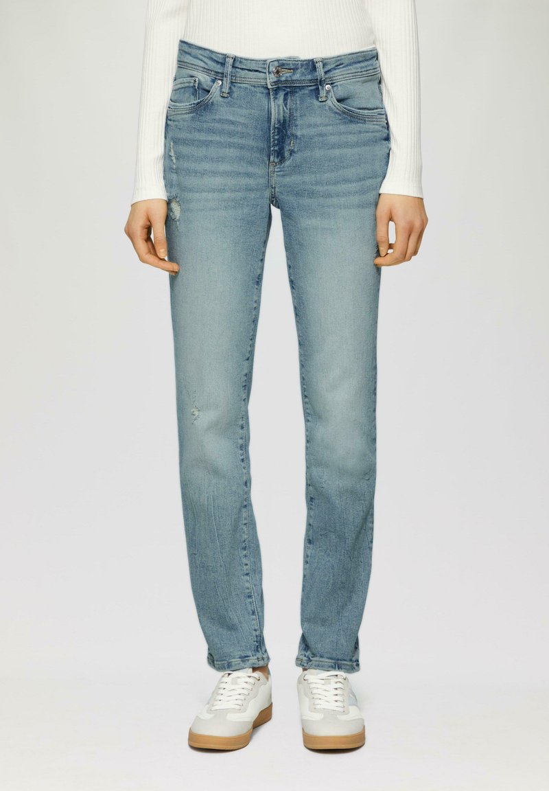 Henkilö, jolla on yllään vaaleansiniset slim fit -farkut, joissa on hieman kulutusta, valkoinen pitkähihaisuu paita ja valkoiset lenkkarit, joissa on kumipohjat, seisoo suorassa.
