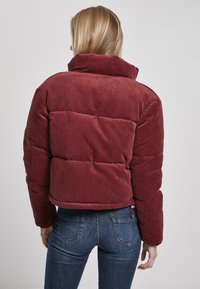 Burgunderrød cordfløyel puffjakke med høy krage og quiltet design, har en cropped passform og ribbet tekstur.