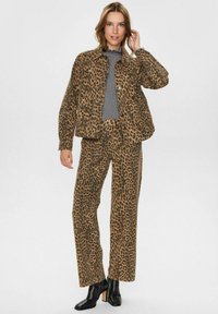 Súprava kabáta a nohavíc s leopardím vzorom v hnedej a čiernej farbe, s klasickým dizajnom, textúrovanou tkaninou a kombinovaná s čiernymi členkovými topánkami.