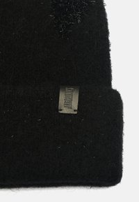 Beanie in lana nera con finitura testurizzata, caratterizzato da un'etichetta in pelle con marchio impresso. Il tessuto presenta una leggera peluria e profondità.