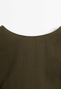 Tissu vert olive avec un col arrondi et des détails de surpiqûres visibles le long du bord.