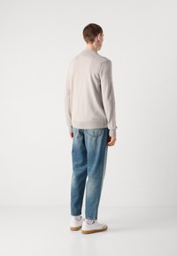 Ljusgrå stickad tröja med ribbade muddar och nederkant, parat med löst sittande blekta blå jeans och vita sneakers. Enkelt design.