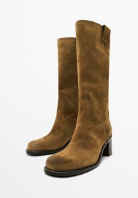Stivali al ginocchio in suede marrone con punta quadrata e tacco spesso. Presentano un design semplice con una superficie liscia e poche parti in metallo.