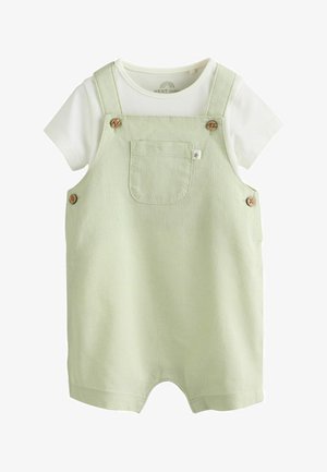 Šviesiai žalias kūdikių smėlinukas be rankovių su priekinė kišene ir mediniais mygtukais, dėvimas ant trumpomis rankovėmis balto medvilninio marškinėlio.