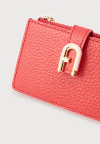 Korallitooni nahast rahakott kuldse ja valge klambriga ning nähtava tõmblukuga heleda halli taustal.