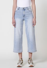 Jeans de tiro alto en azul claro con un diseño acampanado y recortado. Presentan costuras de contraste y un cierre de botón en la cintura.