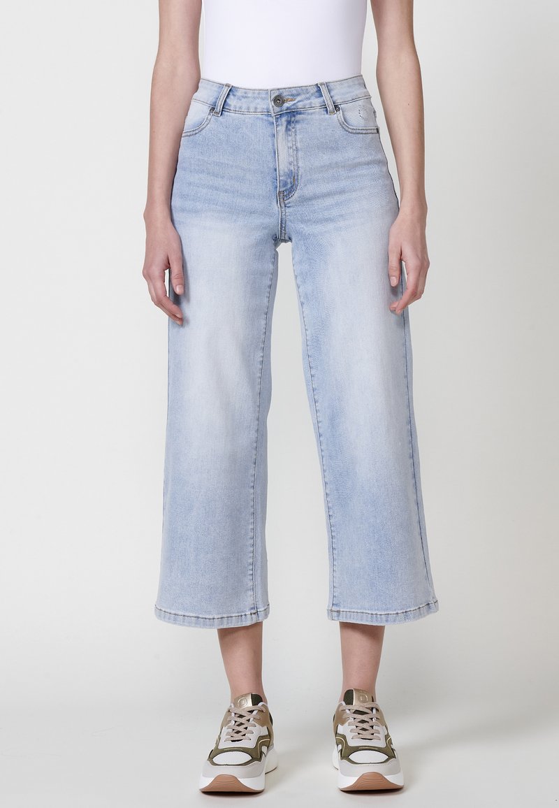Jeans de tiro alto en azul claro con un diseño acampanado y recortado. Presentan costuras de contraste y un cierre de botón en la cintura.