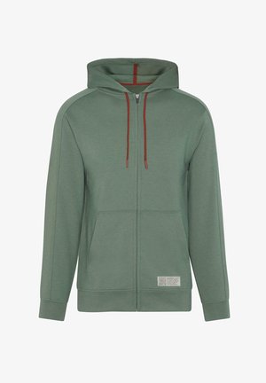 Sudadera verde con cremallera, capucha con cordón, bolsillos frontales y un acabado texturizado. Presenta cordones rojos en contraste y una etiqueta en el dobladillo.