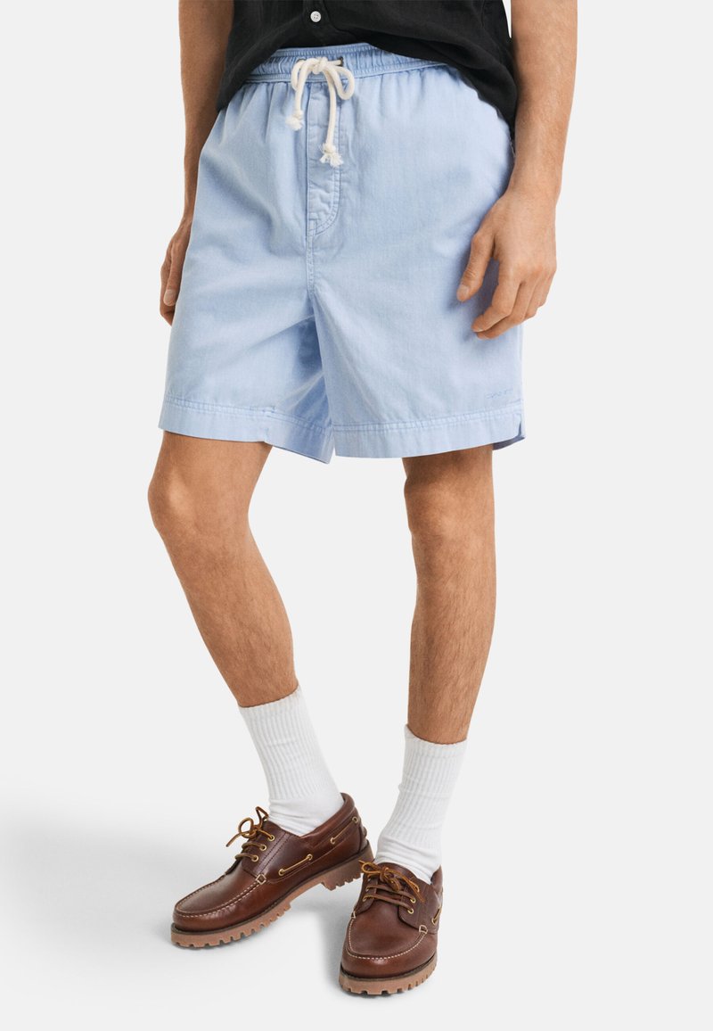Lys blå, letvægts shorts med elastisk talje og snor. Båret med brune lædersko og hvide sokker.