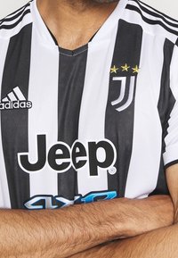 Maglia casalinga della Juventus con strisce verticali bianche e nere, logo ricamato con tre stelle dorate e lettering "Jeep" in nero.