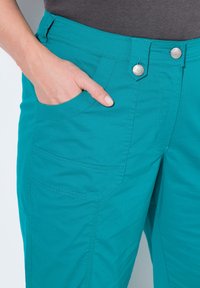 Pantaloni turchesi con una vestibilità slim, realizzati in misto cotone. Presentano una tasca frontale e due bottoni in vita, con cuciture a contrasto.