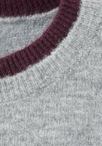 Sivi pleteni pulover s rebrastim bordo ovratnikom. Tekstura izgleda mekano i pahuljasto, prikazujući mješavinu svijetlih i tamnih sivih vlakana.