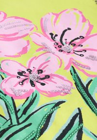 Gėlių audinys su didelėmis rožinėmis gėlėmis ant ryškiai geltono fono. Dekoratyviniai blizgučiai pabrėžia gėlių centrus ir žiedlapius.