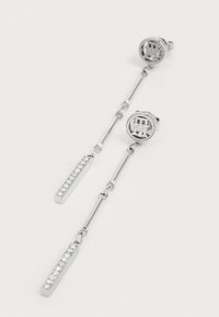 Silver dangling earrings featuring circular top with a geometric design, linked by a chain to a rectangular bar adorned with rhinestones.