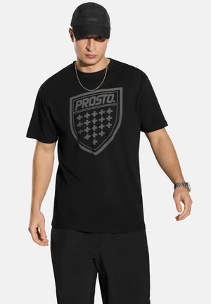 Czarny t-shirt z krótkim rękawem z dużym szarym logo w kształcie tarczy z krzyżami. W komplecie czarna czapka i czarne spodnie. Prosty, nowoczesny design.