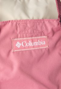 Ροζ ύφασμα με λείο υφή, με λογότυπο Columbia σε λευκό ραμμένο σε ορθογώνιο ετικέτα. Διακοσμητικά στοιχεία περιλαμβάνουν ραφές σε ζιγκ-ζαγκ.