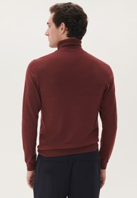 Pulover mulat cu guler înalt de culoare vișinie, cu un design ajustat, guler și mansete ribbate, și o textură netedă, asociat cu pantaloni bleumarin.
