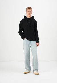 Black hoodie with kangaroo pocket and drawstring hood, featuring embroidered "GAP" logo. Paired with light blue wide-leg jeans and sneakers.