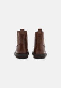 Braune Leder-Ankle Boots mit glatter Textur, runder Zehenform und Zuglasche an der Rückseite. Dicke schwarze Gummisohle mit leichtem Profil.