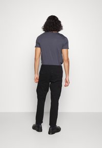 Pantalons cargo noirs et t-shirt gris ajusté. Le t-shirt a des manches courtes ; les pantalons disposent de poches latérales et d'une coupe droite.