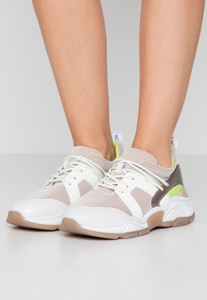 Valkoiset ja vaaleanharmaat verkkomateriaalista valmistetut lenkkarit, joissa on beiget pohjat ja vaaleanvihreät yksityiskohdat, pukeutuneena paljaisiin jalkoihin, kuvattuna edestä ja sivusta.