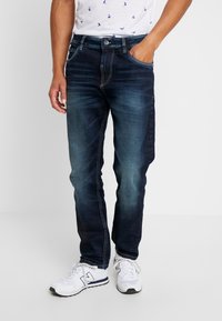 Mörkblå denimjeans med slim fit, som har en traditionell femfickdesign, vita sömmar och en knappgylf.