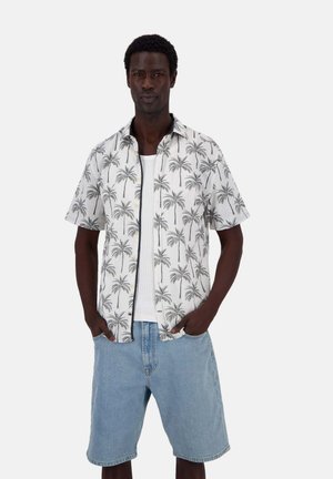 Kurzarmhemd mit weißem Hintergrund, das ein schwarzes Palmenmuster aufweist. Kombiniert mit Jeansshorts, die eine entspannte Passform zeigen.
