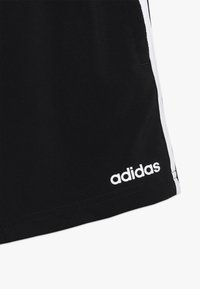 Bermudas deportivas negras con rayas blancas a los lados. Presenta un logo "adidas" blanco en la parte inferior derecha. Fabricadas con un tejido suave y texturizado.