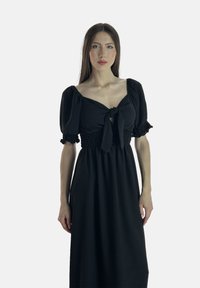 Schwarzes Kleid mit Puffärmeln und einer Bindeschleife am Ausschnitt. Besitzt einen gerafften Taillenbund und einen fließenden Rock. Glatte Textur des Stoffes.