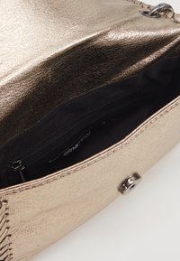 Borsa in bronzo metallico con superficie texture, dotata di un interno nero e tasca con zip. Include una chiusura a scatto e cuciture decorative.