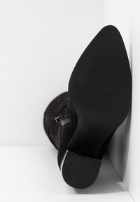 Stivaletto in suede nero con punta affusolata, dettagli con una zip discreta e suola in gomma texturizzata. Finitura liscia e silhouette elegante.