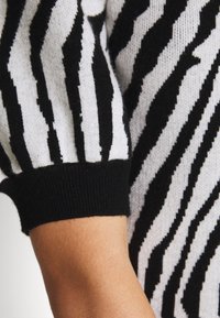 Suéter a rayas blanco y negro con una textura suave. Presenta mangas abullonadas y un puño negro acanalado, que enfatizan sus patrones contrastantes.