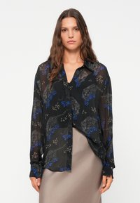 Blusa nera trasparente con una stampa animale blu e grigia. Presenta un frontale con bottoni, maniche lunghe e una vestibilità rilassata. Tessuto liscio.