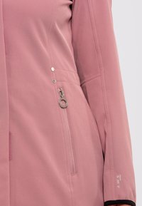 Giacca rosa chiaro con una consistenza liscia, dotata di hardware argentato, tasche laterali con zip e dettagli neri sui polsini.