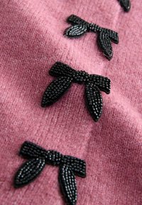 Rosa textil har svarta pärlbroderade bågar. Bågarna har en texturerad yta och är jämnt fördelade över tyget.