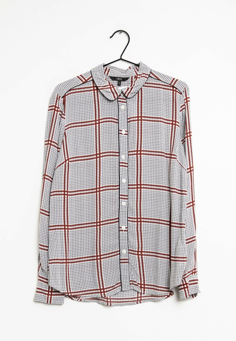 Chemise blanche à manches longues avec petit motif noir et lignes à carreaux rouges, suspendue sur un cintre noir sur fond blanc.