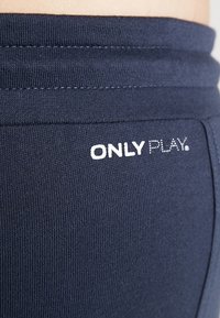 Leggings deportivos azul marino con una textura suave, presentando un logo en letra punteada "ONLY PLAY" en blanco cerca de la cintura.