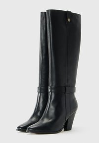 Pair of black leather knee-high boots with pointed toes, block heels, and strap detail around ankles against a light background.