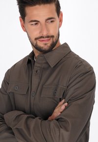 Bruine button-up overhemd met twee voorzakken, gemaakt van een gladde stof. Heeft een klassieke kraag en lange mouwen.