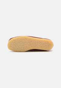 Semelle d'une chaussure avec une base en caoutchouc jaune texturé et un côté maroon lisse. Forme arrondie, motifs de bande de roulement minimalement visibles.