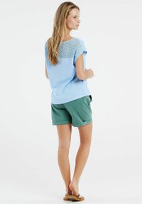 Lichtblauw t-shirt met korte mouwen en een kanten rugdetail, gecombineerd met groene shorts. De outfit heeft een ontspannen pasvorm en een casual ontwerp.