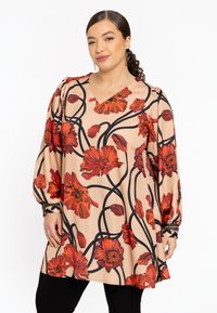 Lang beige bluse med et blomstermotiv med røde blomster og sorte konturer. V-hals, lange ærmer med rynkede detaljer ved manchetterne.