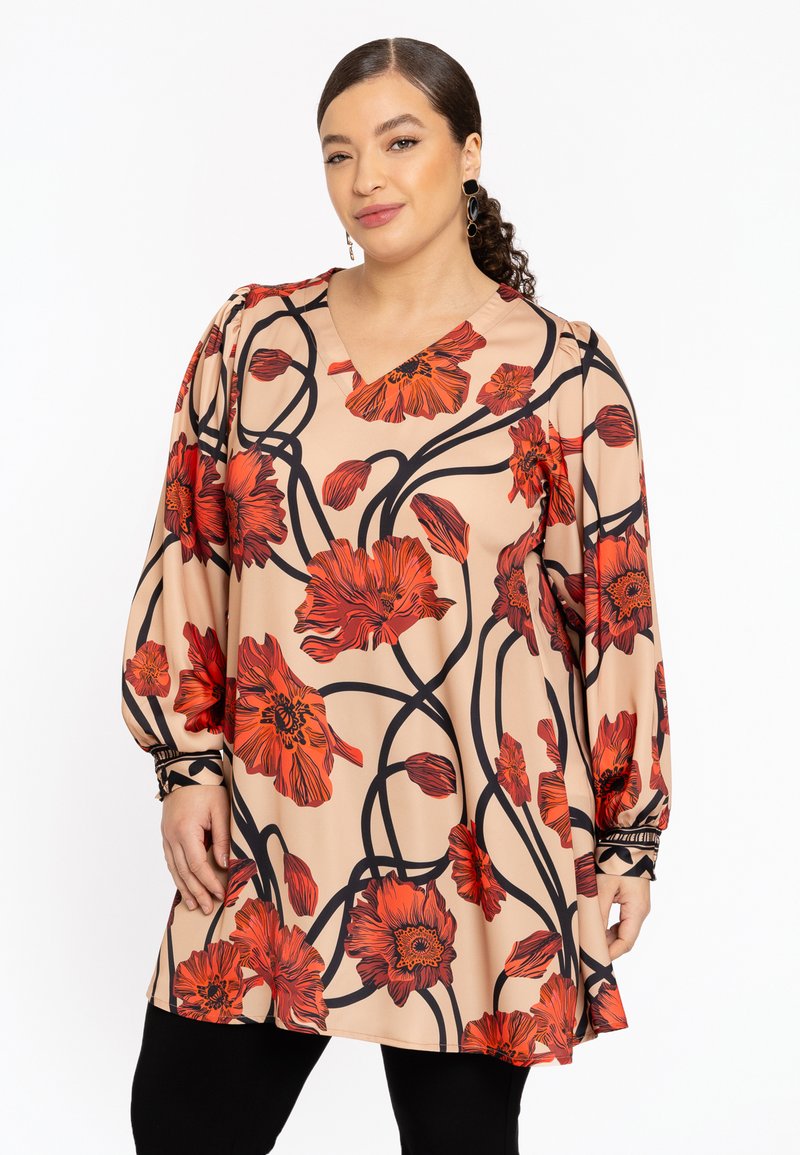 Lang beige bluse med et blomstermotiv med røde blomster og sorte konturer. V-hals, lange ærmer med rynkede detaljer ved manchetterne.