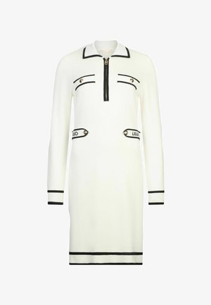 Biała dzianinowa sukienka z kołnierzykiem, zapinana z przodu na zamek błyskawiczny, z czarnymi akcentami. Posiada dwie dekoracyjne kieszenie z logo oraz ryflowane mankiety i dół.