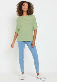 Maglietta verde chiaro a maglia larga con maniche ampie, abbinata a jeans skinny blu chiaro e sneakers bianche. La maglietta presenta un motivo testurizzato.