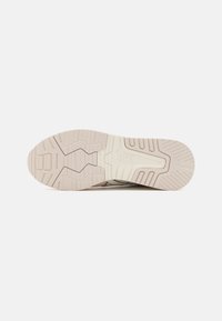 ASICS sneaker with a beige rubber sole featuring a textured pattern and grooves for grip. Design includes a logo on the side.