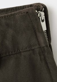 Gros plan sur un tissu marron foncé avec une fermeture éclair métallique argentée partiellement fermée le long du bord d'un vêtement.