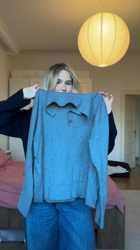 Sivá košeľa s dlhým rukávom z jemnej látky s preklápacím golierom, detailmi na gombíky a voľným strihom. Celá košeľa má jemnú textúru.