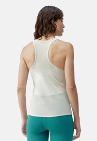 Hvit sports tank topp med racerback-design, som har en glatt tekstur og en subtil logo detalj bak, sammen med teal leggings.