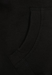 Tessuto di cotone nero con un dettaglio di tasca applicata. Texture liscia e cuciture a vista. Nessun motivo o accento aggiuntivo visibile.